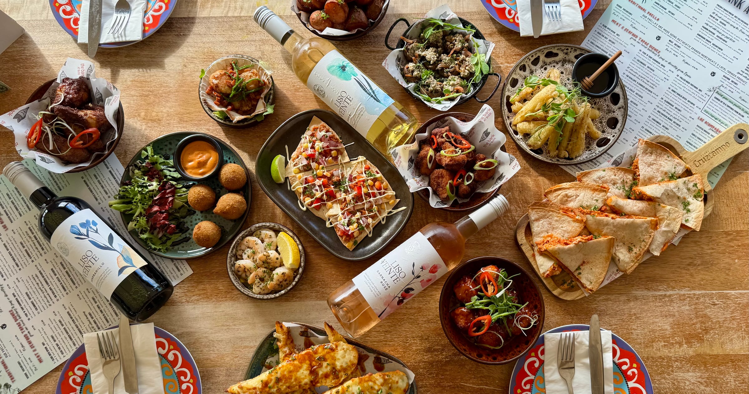 An overhead spread of Spanish-Cornish tapas — small plates, paella, quesadillas, wine and sangria — laid out for sharing on the table at The Bank at Bude in Cornwall