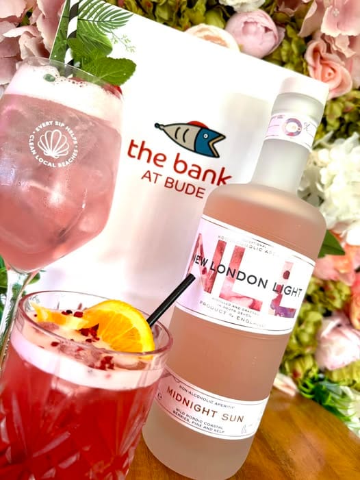 Pink cocktails on a marble tabletop beside The Bank at Bude branded napkin